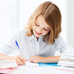 ein Mädchen sitzt umgeben von Büchern an einem Tisch und schreibt mit einem Kugelschreiber